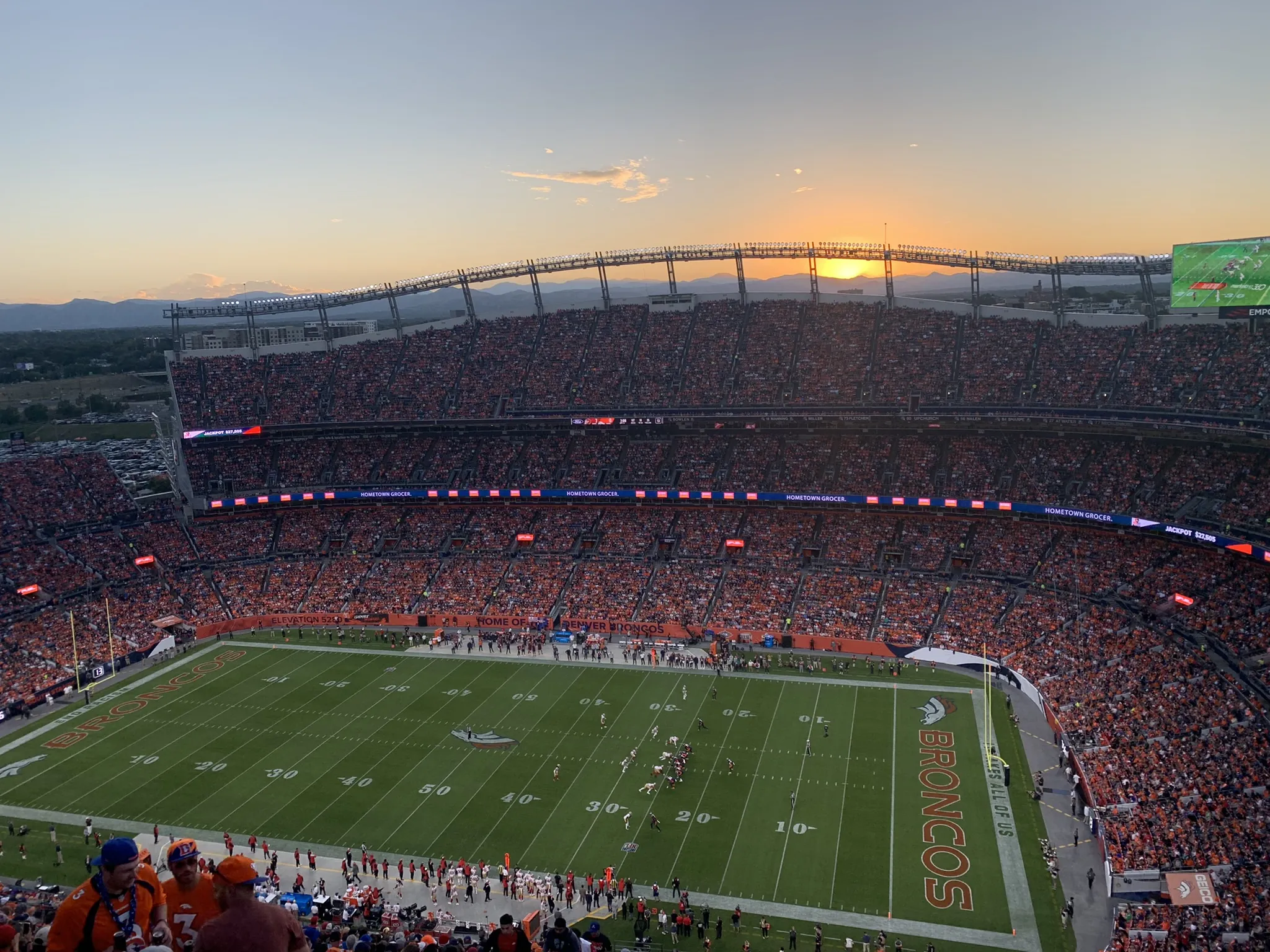 The sun setting over the mountains behind a packed Empower Field at Mile High